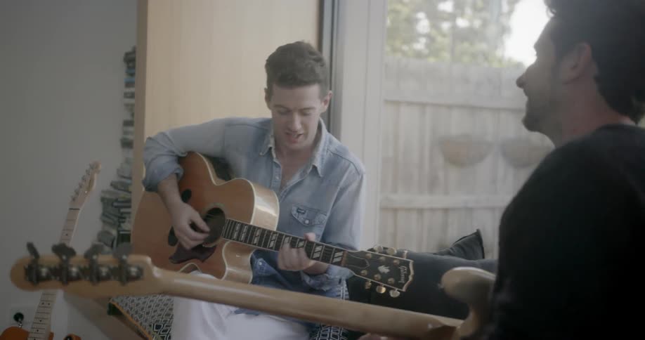 Two men converse and play guitars