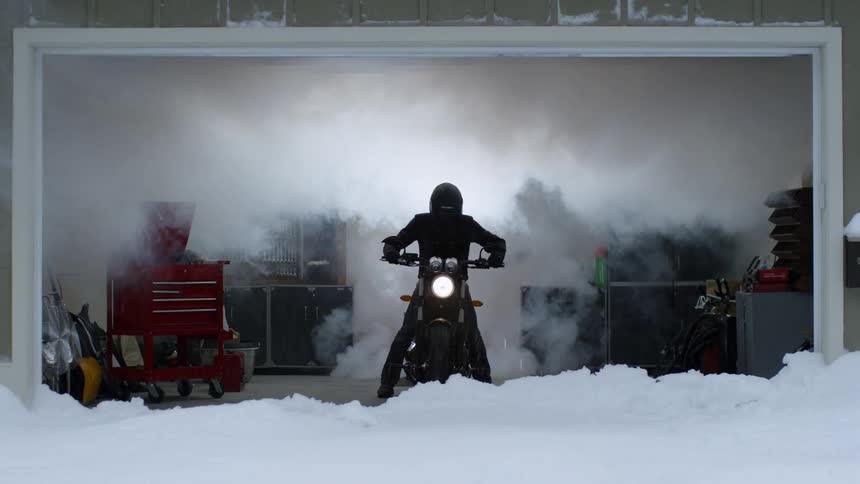 A man on a motorcycle is revving the engine inside his garage in winter