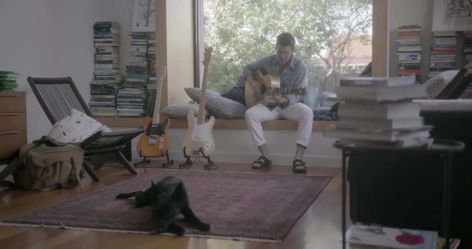 A man sits by the window playing guitar