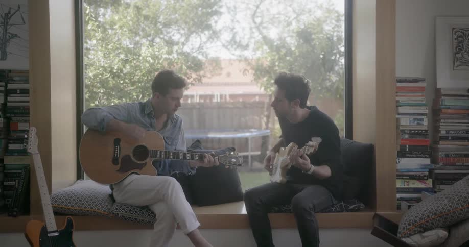 Two men are sitting in a window playing guitars and singing