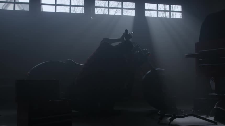A man squats down by a motorcycle in a garage with his tools