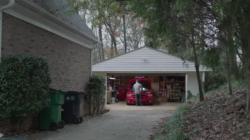 A man works on his car in the garage with the door open