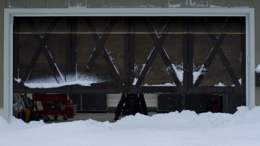 Garage door opening as it's snowing while a motorcyclist waits to exit
