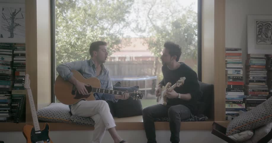 Two men converse and play guitars