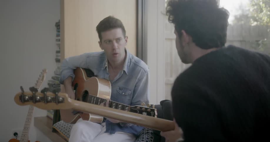 Two men converse and play guitars
