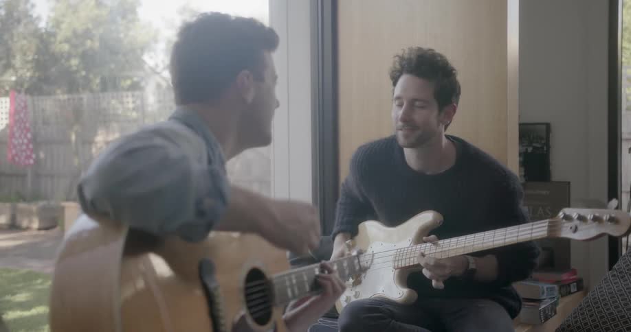 Two men play guitar on a window bench