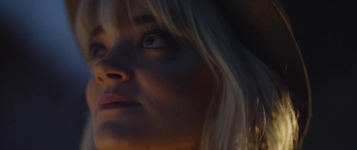 A woman opens her eyes and smiles as she stands outside at night