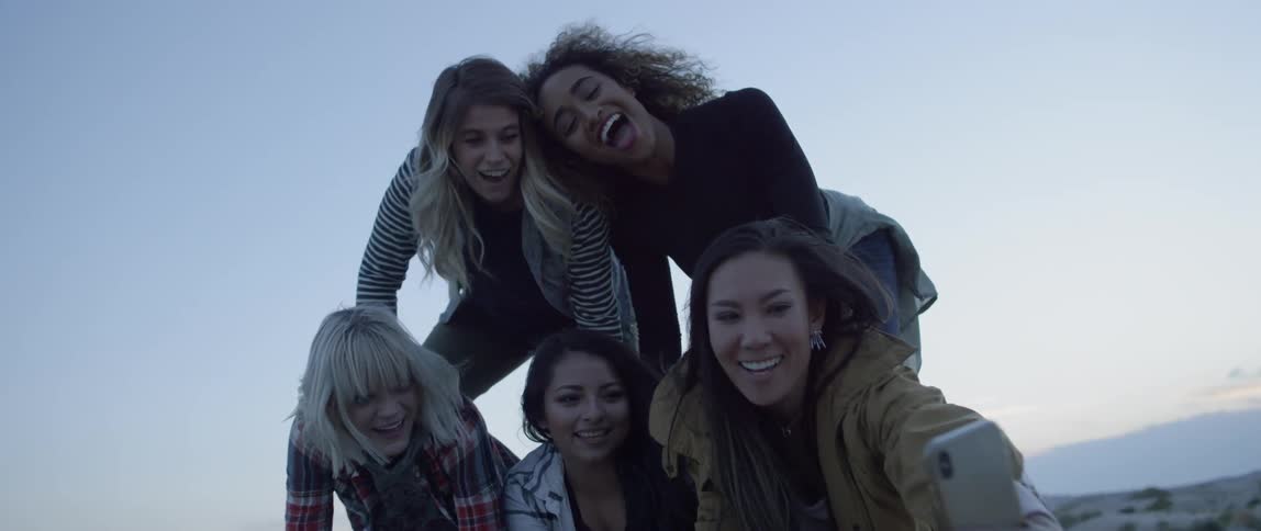 Five women making a human pyramid in a sandy area and taking a selfie