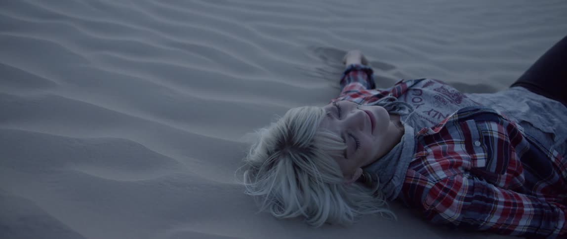 A woman is lying on a sand dune and smiling