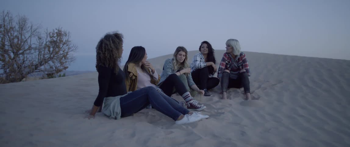 A group of women sit on a sand hill and talk