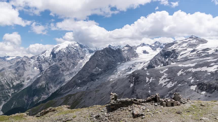 Clouds float over snowy mountains behind building ruins