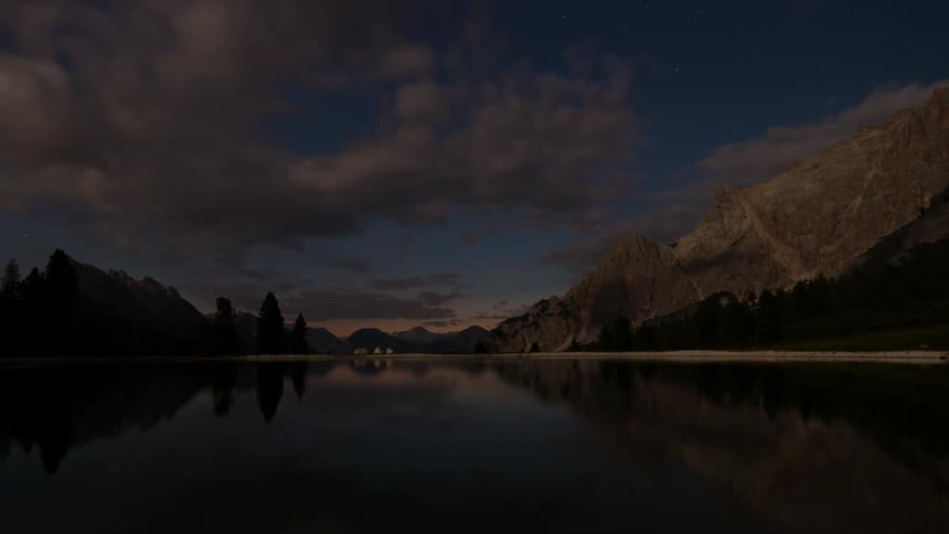 Sunset and moonrise by a reflective mountain lake