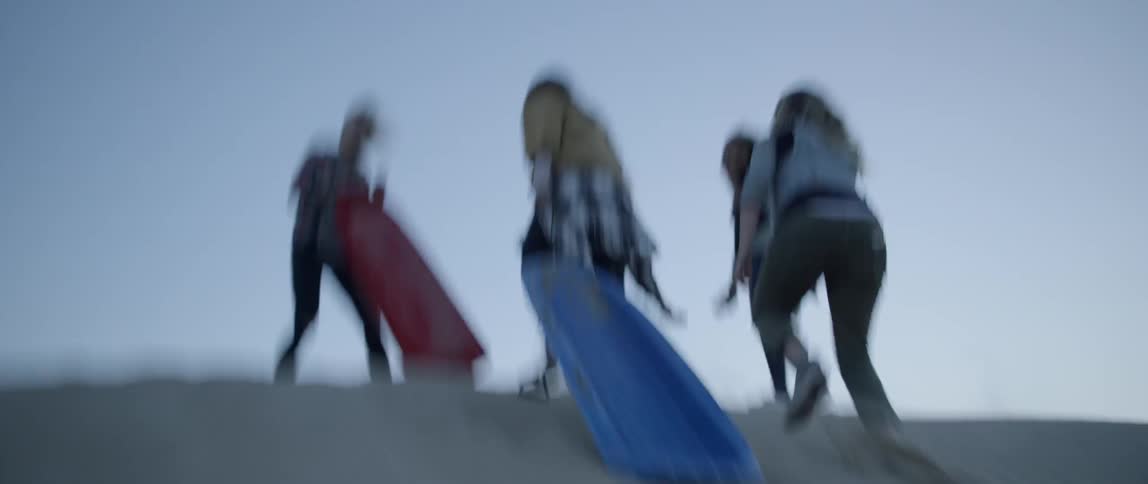 Several women run up a sand hill and two hold sleds