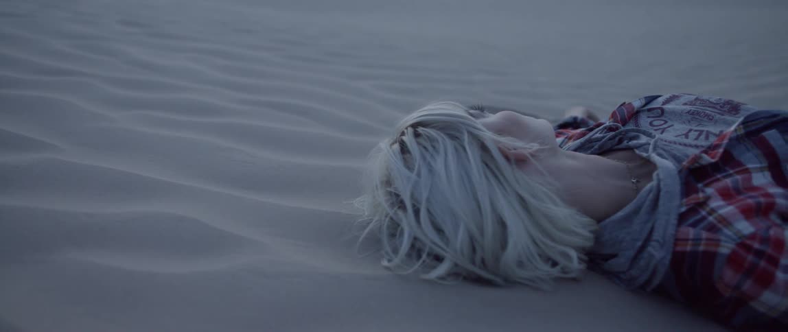 A woman lays on her back in the sand with the wind blowing in her hair