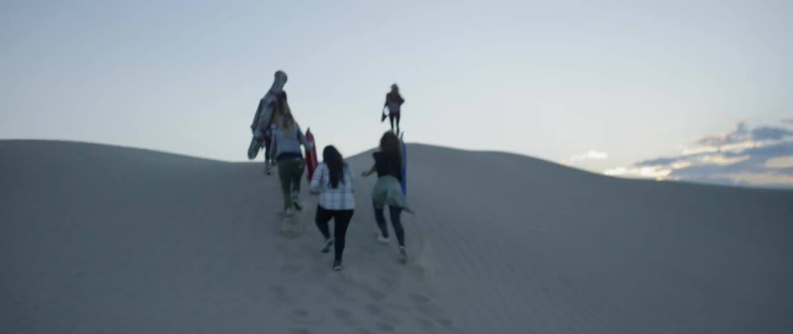 A group of women climb up a sand hill