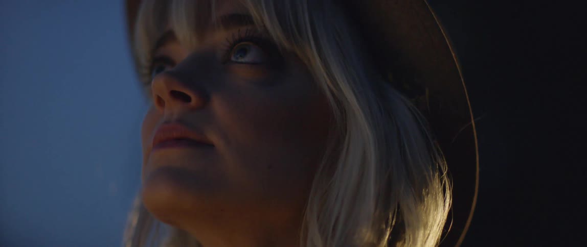 A blond haired women looks upwards at night