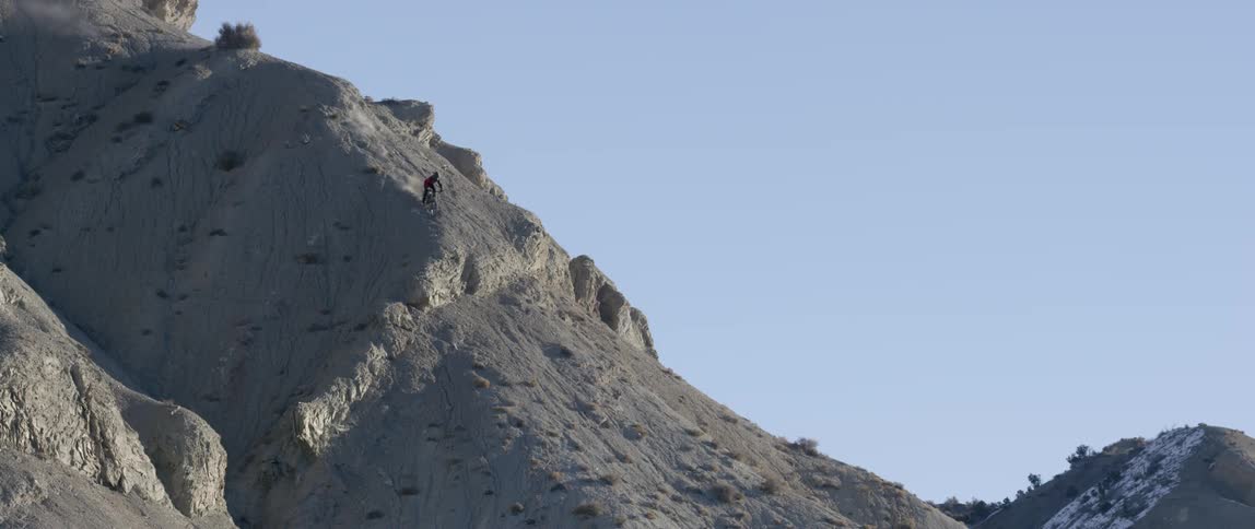 A person bikes down a steep, sandy hill