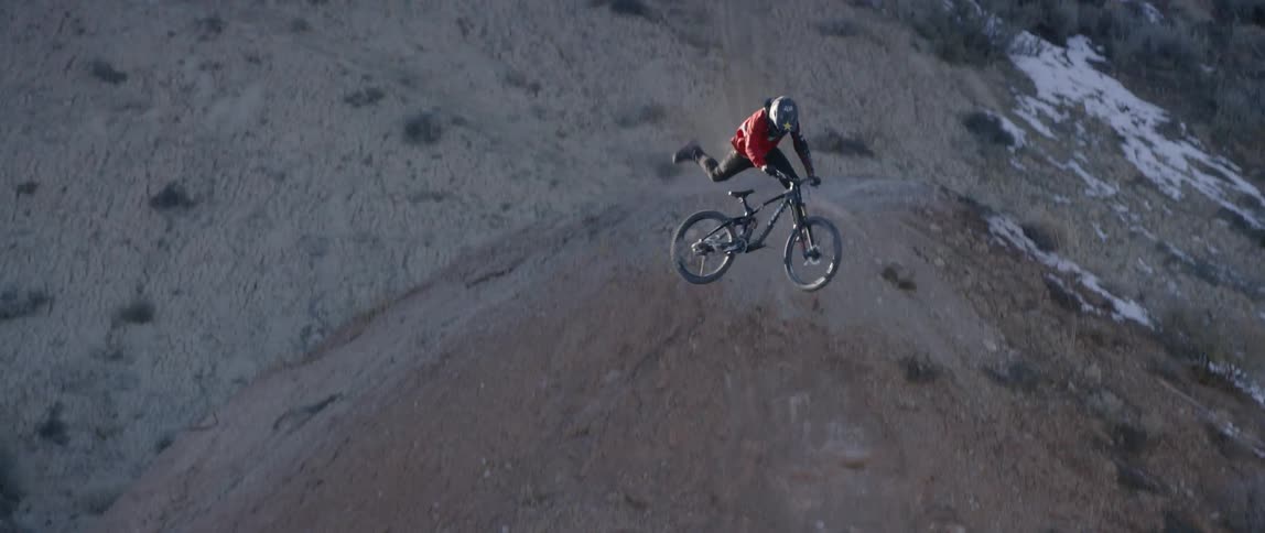 A bicyclist does a trick while jumping over a dirt hill