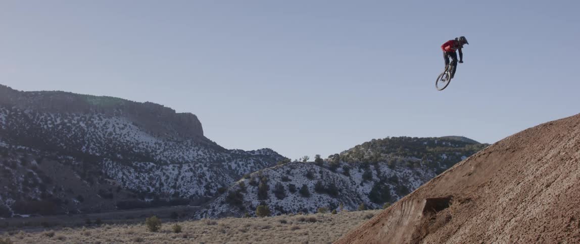 A bicyclist jumps and does a trick on a dirt hill