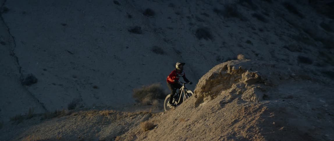 A person is riding a bike along a mountain ridge and does a backflip off a jump