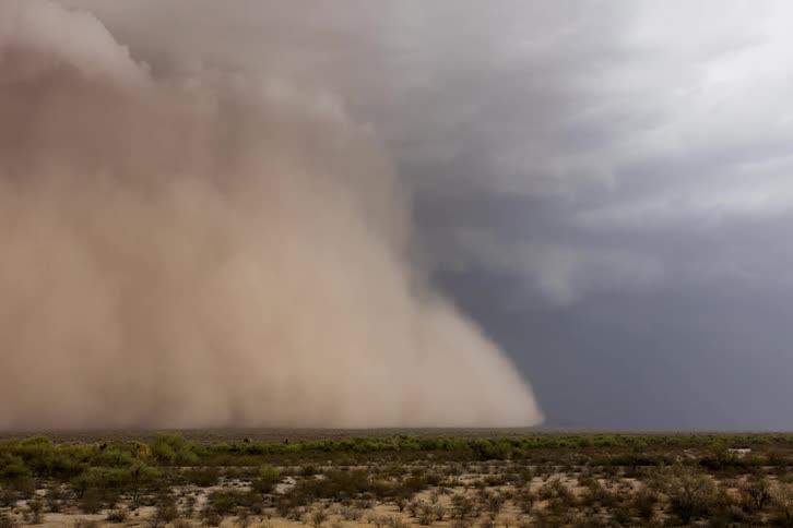 A dust storm moves across a rural field