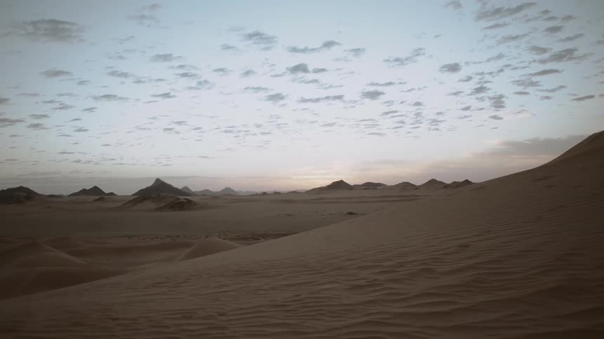 Clouds dot the sky over sand dunes at sunset