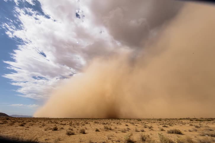 A sand storm is moving across the desert in daylight