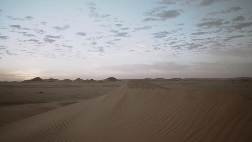 Clouds dot the sky over sand dunes at sunset