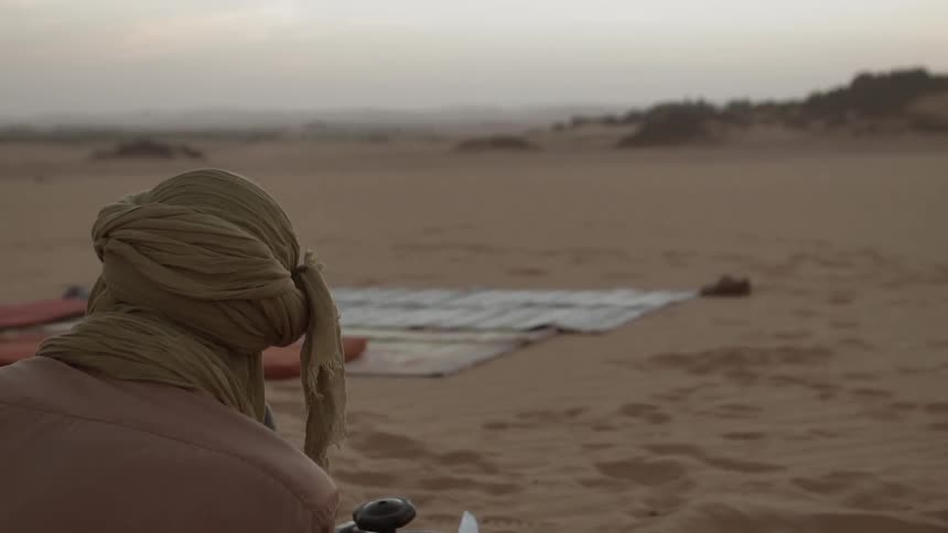 A man sits in the desert by a fire