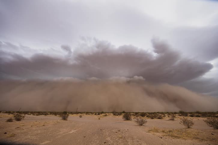 Dust storm rapidly approaching over a field