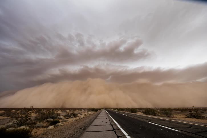 Cars drive down a road as a dust storm expands and covers the land