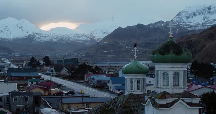 An eagle sits perching on a church cross in a mountain village at dusk