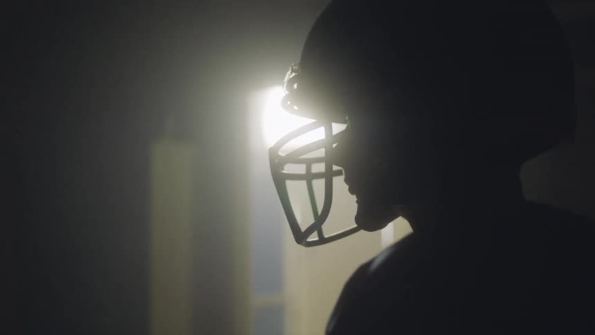 Football player stands in a dark room with a lit door before him