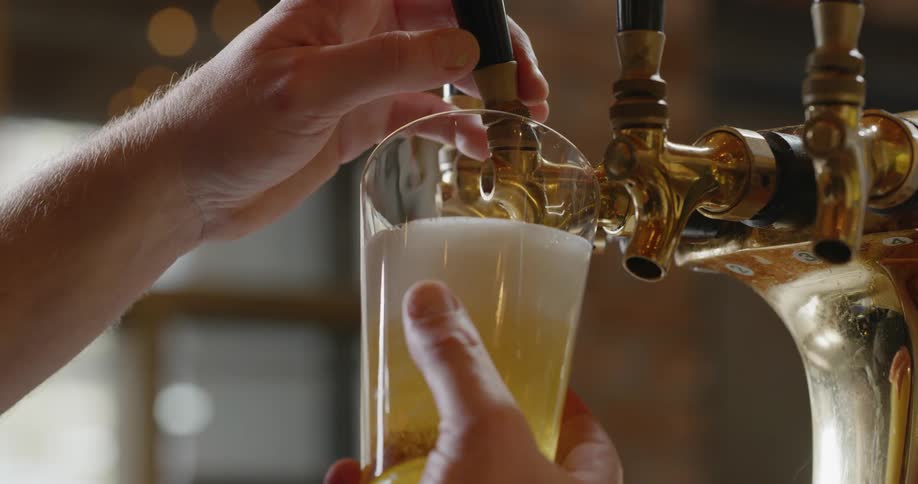 Someone is pouring a beer into a pint glass at a bar