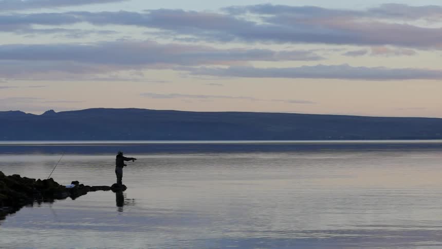 Man fishes on a lakeshore at sunset