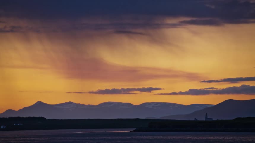 An ocean beneath rainy clouds at sunset