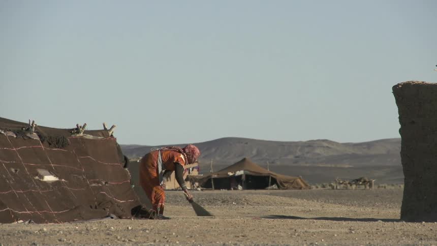 A woman is sweeping the ground outside her hut on a sunny day