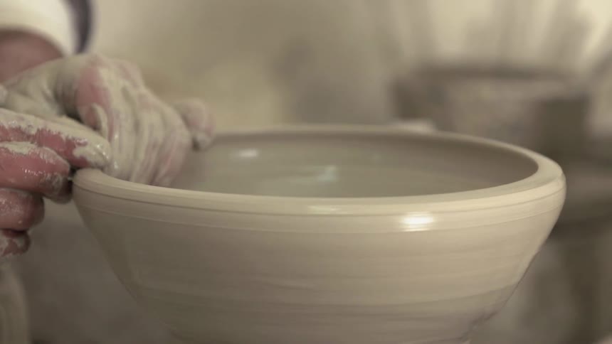 Hands shape a bowl on a pottery wheel