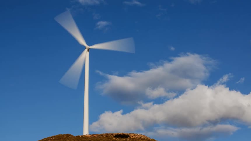 A time lapse of a wind turbine spinning as clouds go by