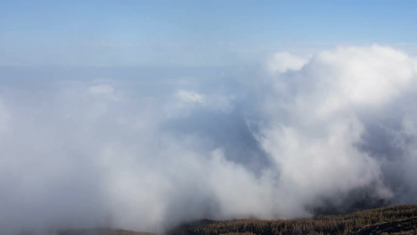 Clouds are billowing and drifting over a mountainside during the day