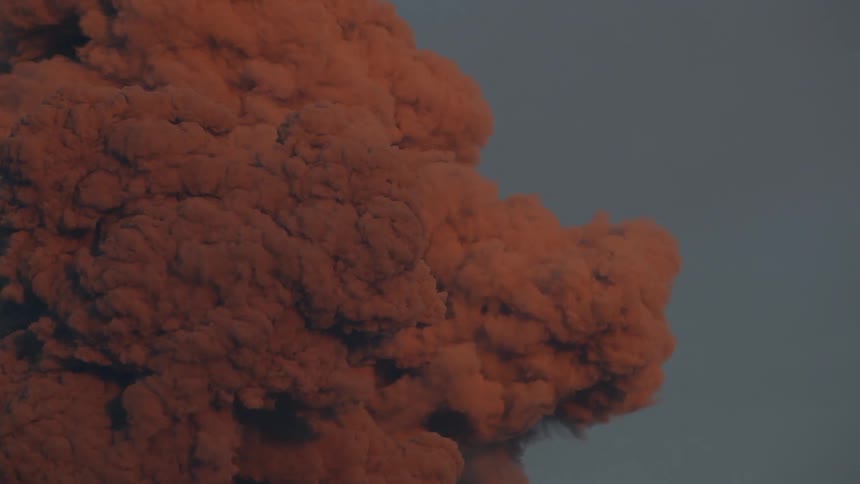Red smoke billows against a cloudy sky