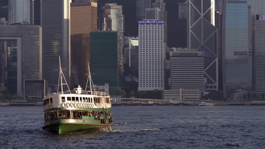 A ferry boat is navigating across a harbor in a metropolitan area during the day