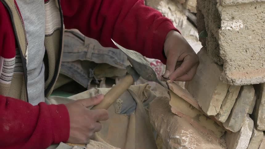 A man uses a pick axe to chisel