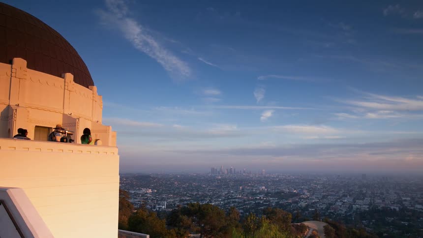 Tourists are viewing a city from a building as day turns to dusk
