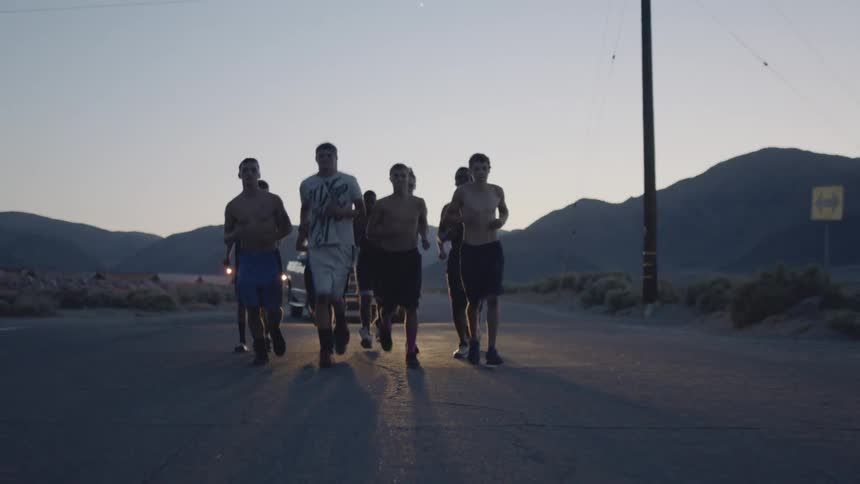 Group of people running on a road at sunset as a car follows with its lights on
