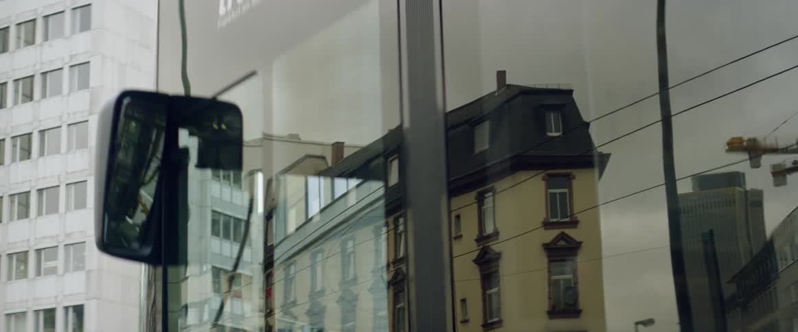 A bus window is reflecting the buildings around it as it drives