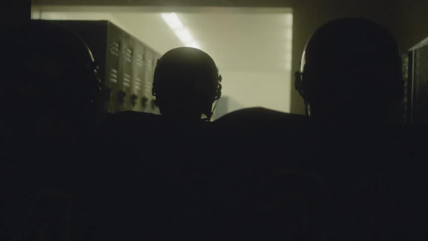 Three football players in uniform walk into a locker room