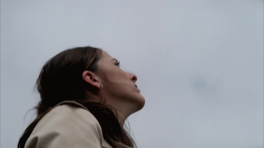 The wind blows a woman's hair as she watches a jet fly overhead