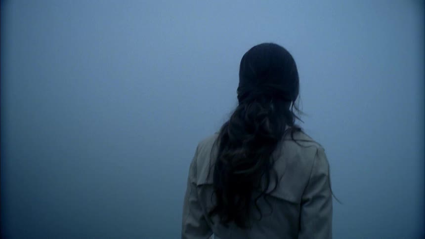 A woman in a trench coat stands out in the fog