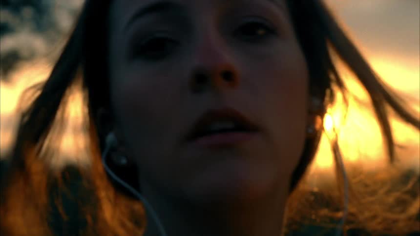A woman wearing earbuds brushes her hair back with her hands